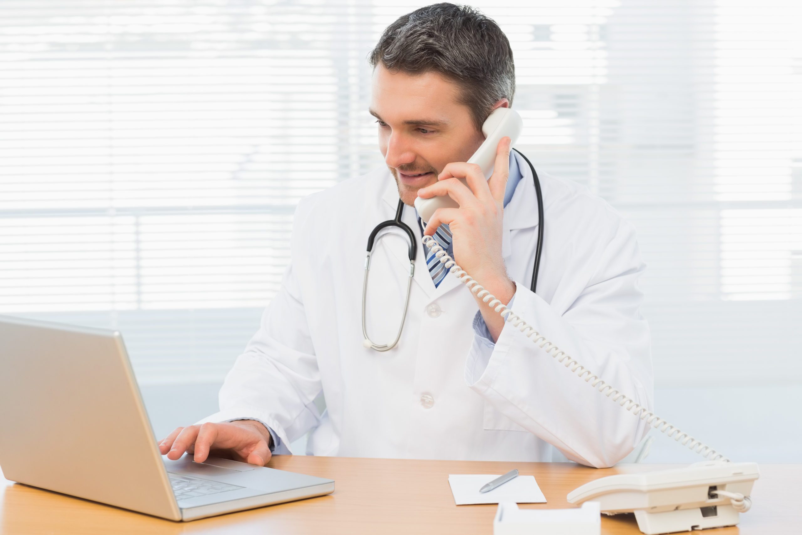 Concentrated male doctor using laptop and phone in the medical office