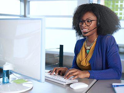 Friendly african american casual call center emplyee working at a desktop computer in a modern withe office